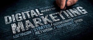 Hand pointing a pen toward bold text reading "Digital Marketing" surrounded by strategy, network, and marketing concept keywords on a dark textured background.