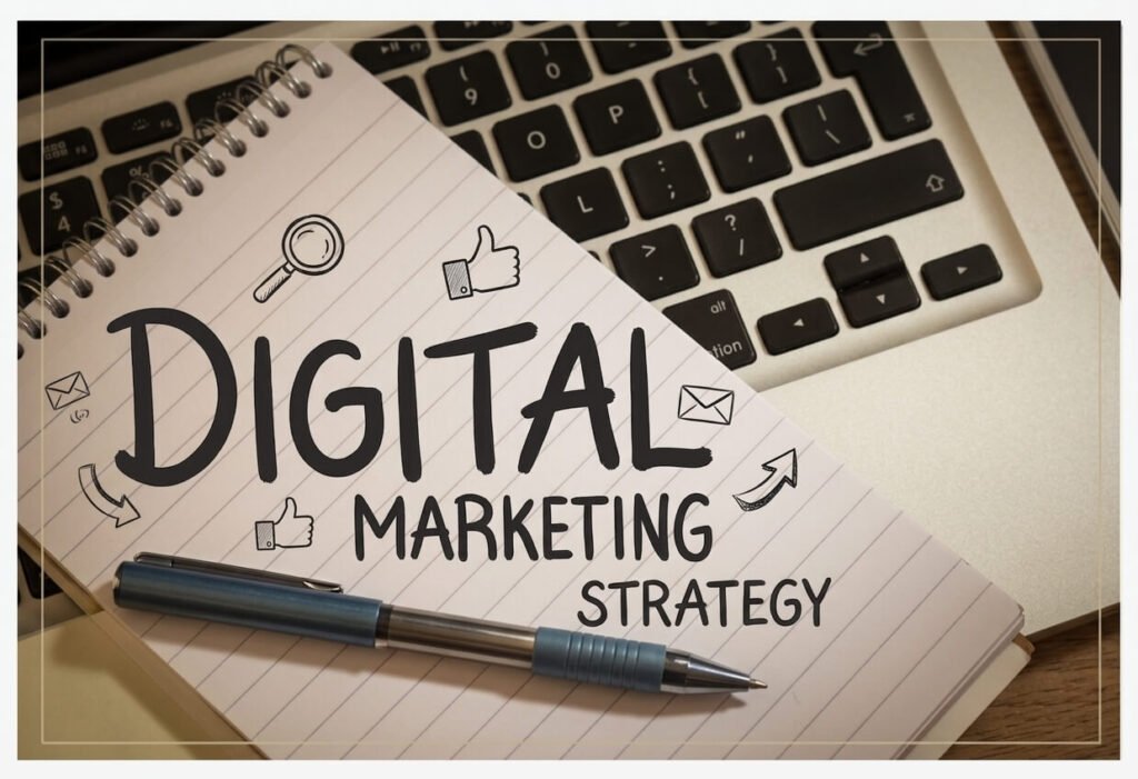 Hand-drawn text reading "DIGITAL MARKETING STRATEGY" on a lined spiral notebook, accompanied by doodles of a magnifying glass, thumbs up, emails, and arrows. A blue pen rests on the notebook, which is placed on a laptop keyboard.